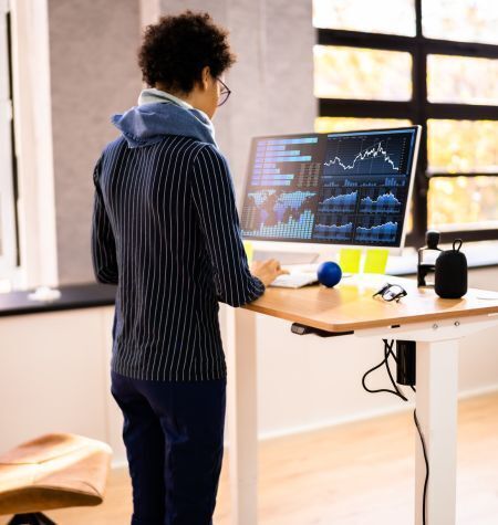 Woman Using Adjustable Height Desk to Stand In Office Using Computer